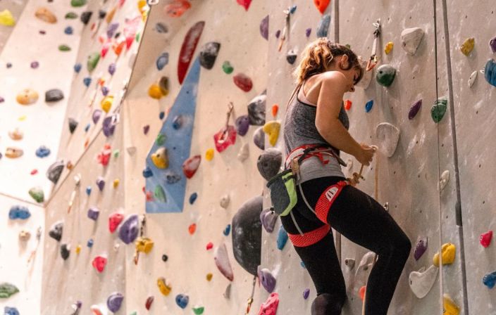 Eine junge Frau an einer Kletterwand hängt ihren Karabiner ein - Symbolbild für Kontrolle und Sicherheit.