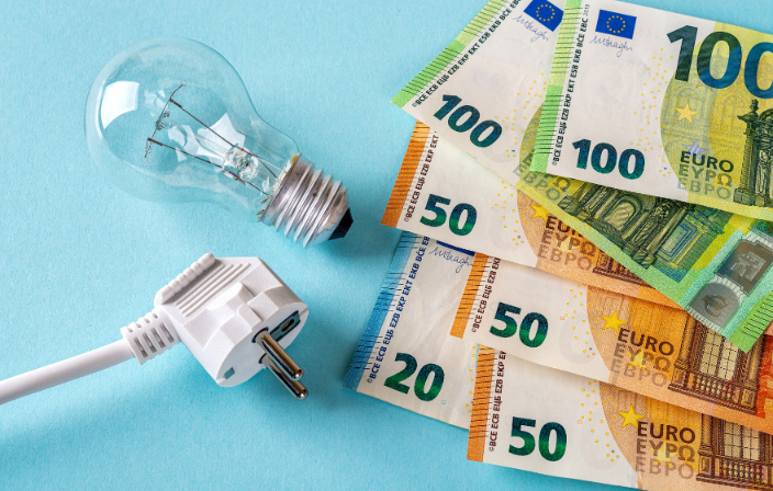 Neben einem Stromstecker und einer Glühbirne liegt ein Bündel Geldscheine - Symbolbild für Energiekosten
