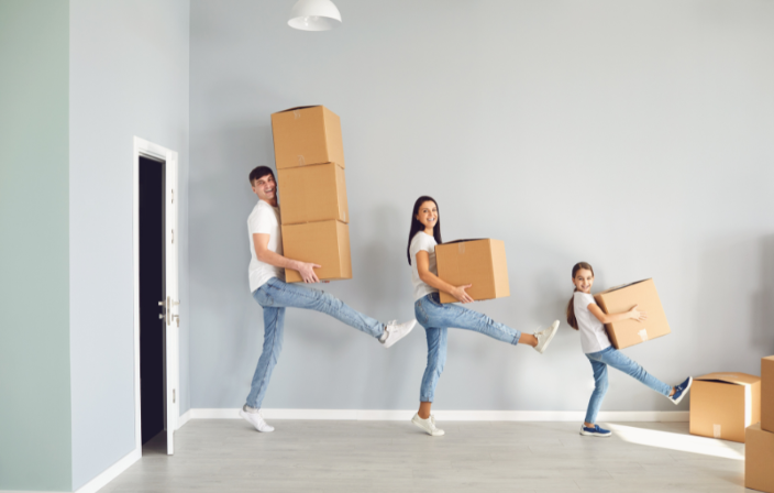 Eine junge Familie, Vater, Mutter und gut 10 jährige Tochter, tragen spielerisch im Stechschritt Kartons aus der Wohnung.