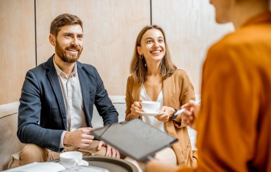 Ein Pärchen, ein Mann und eine Frau, sitzen am Sofa bei einem Kaffee und hören einem Energieberater zu.